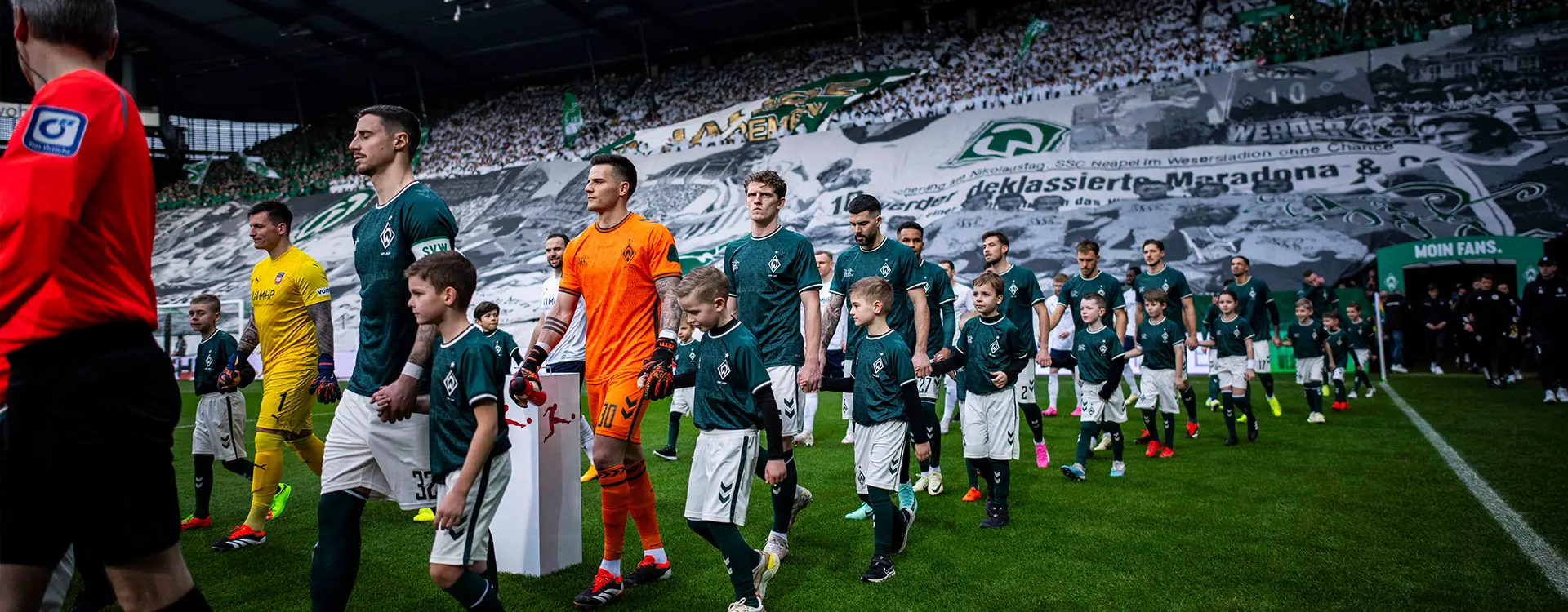 Spieler des SV Werder Bremen und des 1. FC Heidenheim betreten das Spielfeld und halten die Hand von Nachwuchsspielern in den gleichen Trikots. (Foto)