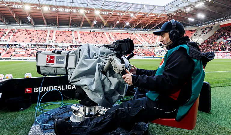 Ein Kameramann auf einem Drehstuhl führt die Kamera an der Seitenlinie des Spielfeldes. (Foto)