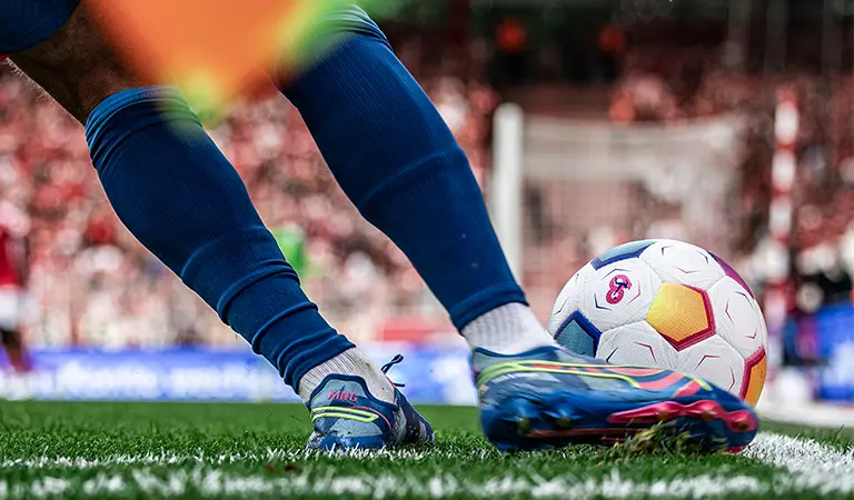 Nahaufnahme eines Fußballspielers, der den Ball mit den Zehen berührt, mit einem Tor im Hintergrund. (Foto)