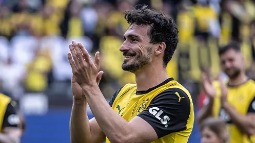 Mats Hummels klatscht in seinem schwarz-gelben Trikot, im Hintergrund sind Teamkollegen und Fans zu sehen. (Foto)
