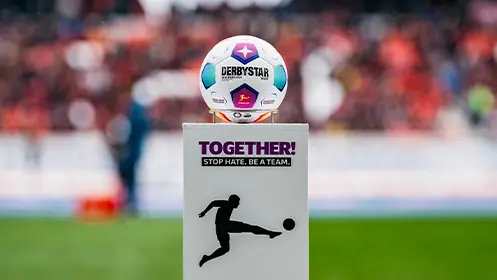 Ein Fußball, der auf einem Podest platziert ist, der Hintergrund ist unscharf mit Menschen, die auf der Tribüne sitzen. (Foto)