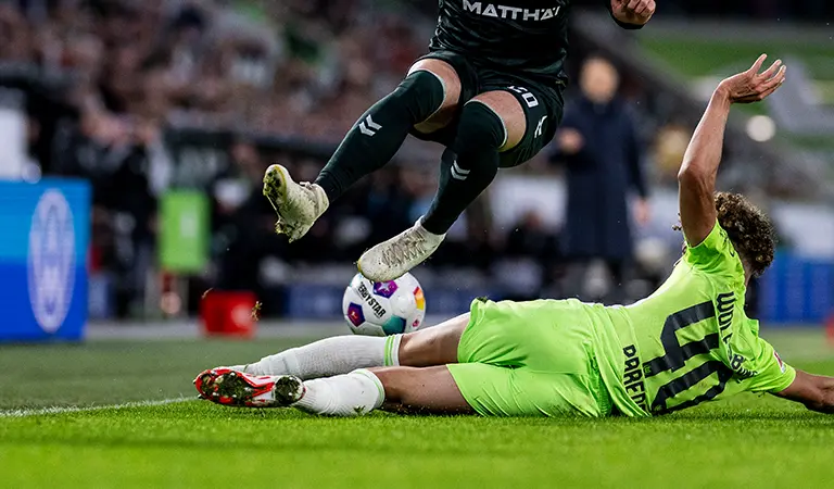 A goalie in a green jersey, sliding on the floor to defend from an attacking adversary player. (Photo)
