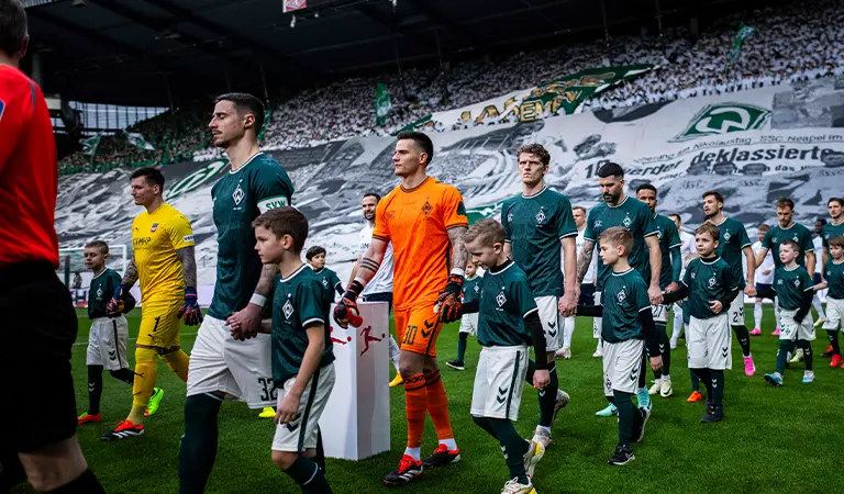 SV Werder Bremen and 1. FC Heidenheim players walking out onto the field, holding hands with junior players in the same jerseys. (Photo)