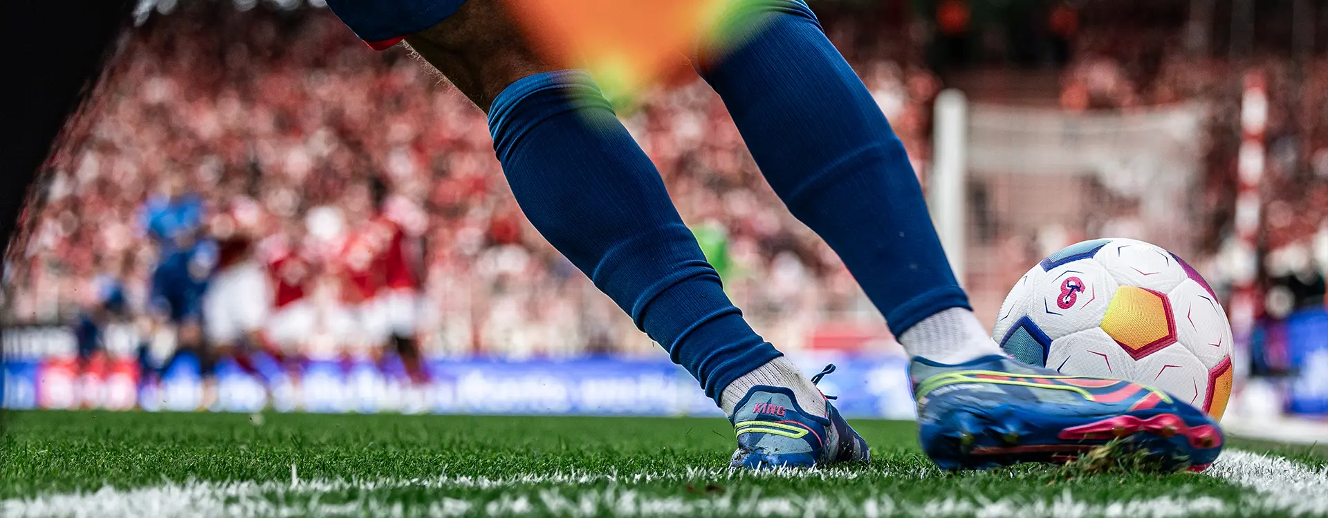 A closeup of a football players feet while he toes of the ball, with a goal visible in the background. (Photo)