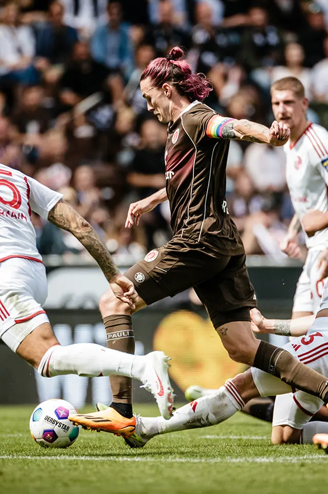 Jackson Irvine with pink dyed hair in action on the footballfield in his FC St. Pauli jersey, running with a football. (Photo)