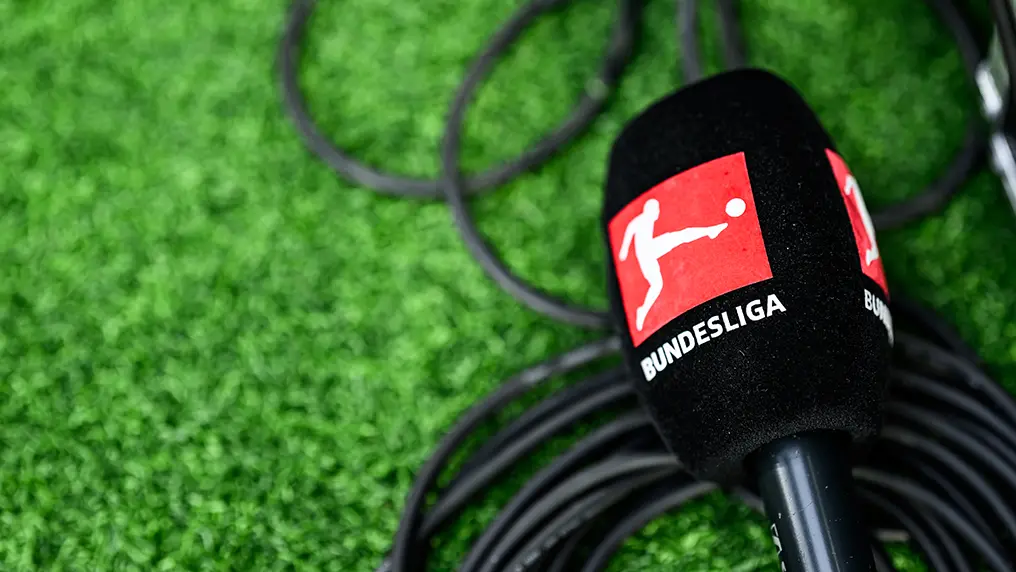 A microphone with the red Bundesliga logo embued, laying on the turf of the field. (Photo)