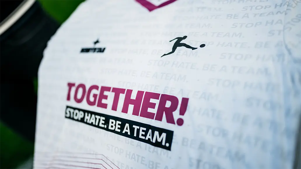 A closeup of a white jersey with "TOGETHER! STOP HATE. BE A TEAM." on it. (Photo)