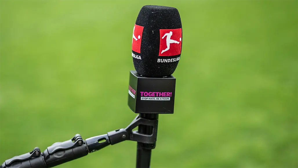 A microphone with the Bundesliga logo and the TOGETHER! STOP HATE. BE A TEAM." logo below, with green turf in the background. (Photo)