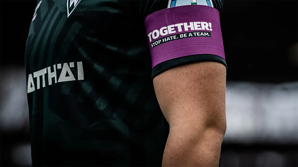 A football player in a black jersey with the purple "TOGETHER! STOP HATE. BE A TEAM." armband on his beefy, freckled biceps. (Photo)