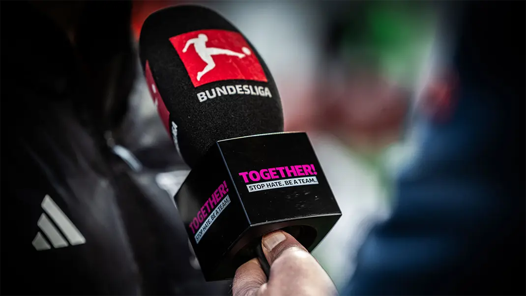Closeup of a reporters hand with the microphone extenden and the "TOGETHER! STOP HATE. BE A TEAM." logo visible on it. (Photo)
