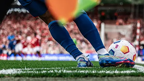 A closeup of a football players feet while he toes of the ball, with a goal visible in the background. (Photo)