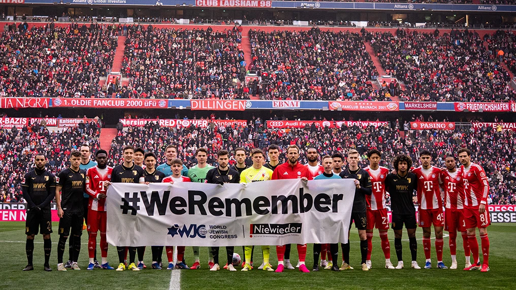Spieler des FC Bayern München und des FC Augsburg halten am 21. Erinnerungstag einen Banner mit der Aufschrift "#WeRemember" hoch (Foto)